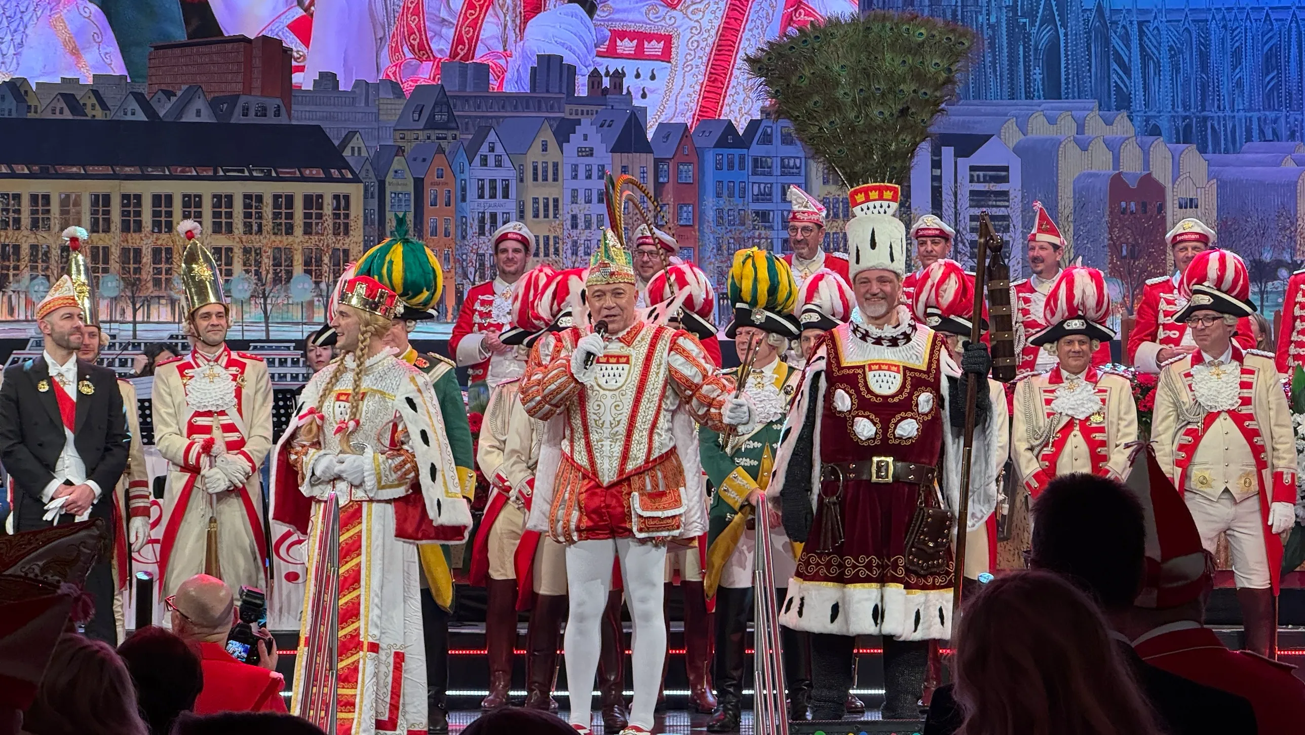 Bühnenprogramm mit Prinz, Bauer und Jungfrau des Dreigestirns sowie Korps auf der Bühne vor Kölner Stadtkulisse