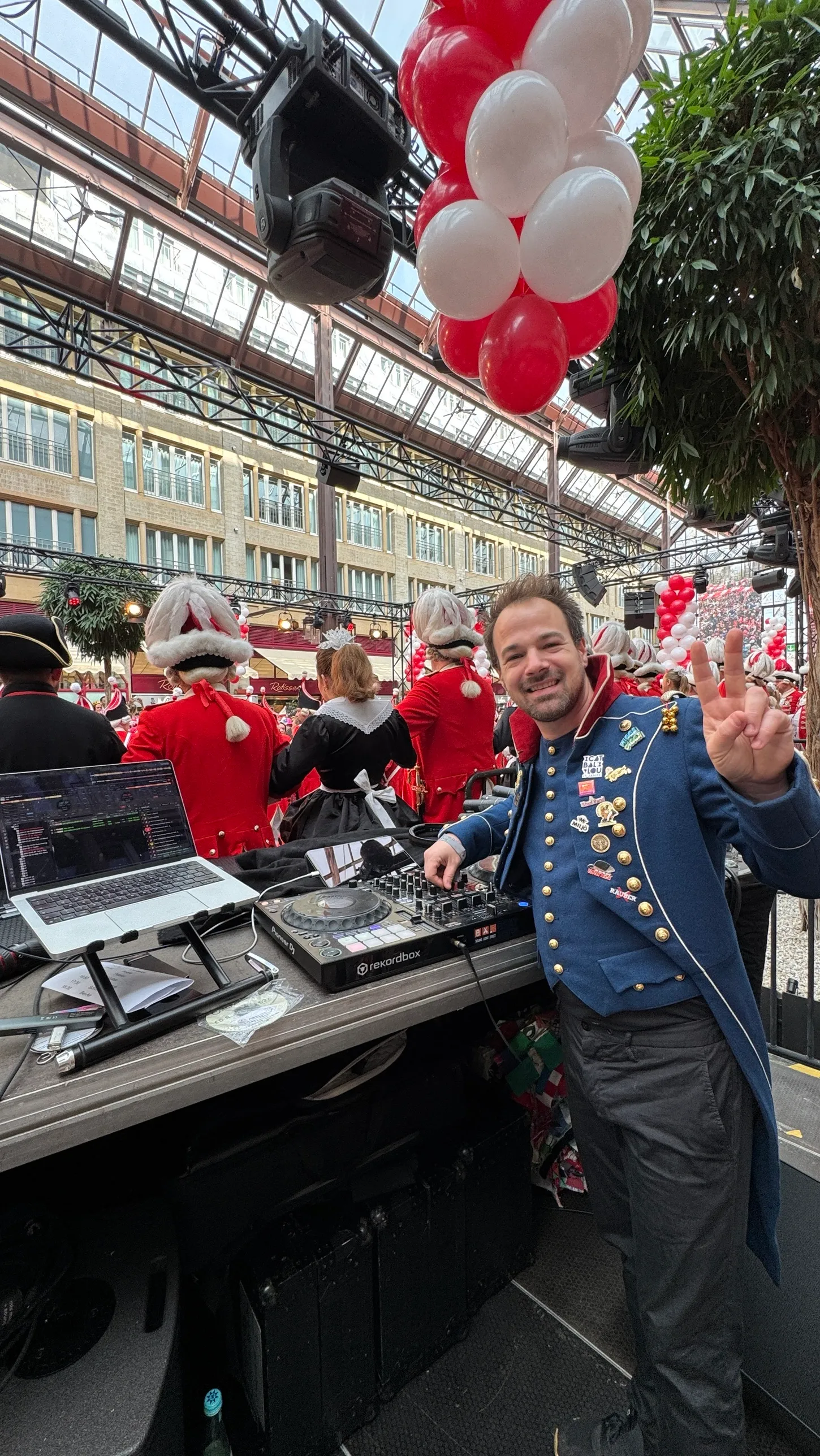 René Braun am DJ-Pult mit Laptop und Controller, dahinter das Korps der Roten Funken unter dem Glasdach der Passage